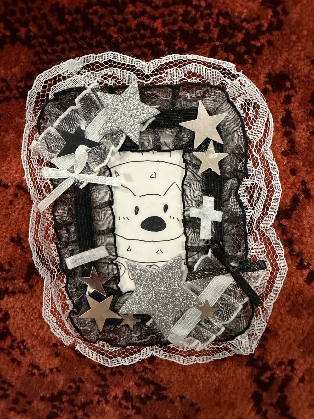 Front view of a handmade black-and-white lace card frame decorated with silver stars and ribbon, holding a hand-drawn puppy card.